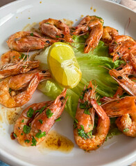 Plate of grilled shrimp arranged in circular pattern. Cooked to a vibrant pink color and are garnished with fresh parsley and lemon. Bed of lettuce, adding a touch of freshness. Mediterranean dish