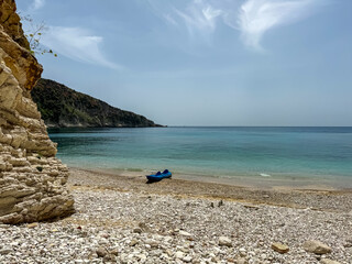 Blue kayak is pulled up on sandy shore of secluded pebble Filikuri Beach in Himare, Albania. Crystal-clear turquoise water of Ionian Mediterranean sea. Serene atmosphere. Seaside summer vacation