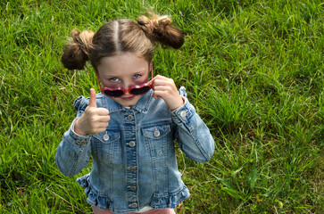 Cool kid girl looks over the sunglasses and thumbs up.