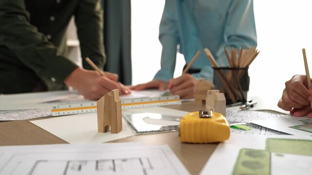 Smart architect and safety engineer discussion about building blueprint on table with architectural document, measurement tools and wooden block scatter around at modern office. Closeup. Delineation.