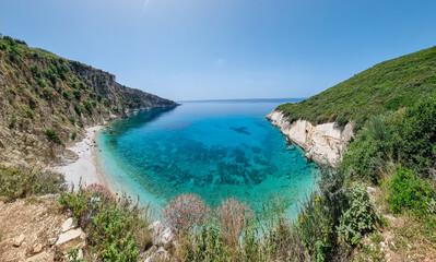 Fototapeta premium Aerial view of secluded pebble Filikuri Beach surrounded by dramatic cliffs in Himare, Albania. Crystal-clear turquoise water of Ionian Mediterranean sea. Peaceful atmosphere. Seaside summer vacation