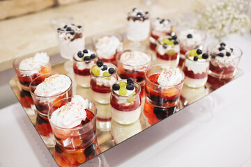 Desserts in jars with a creative presentation. Jelly with whipped cream and fruit served in an elegant way. A delightful treat idea for guests, displayed on a mirrored tray.