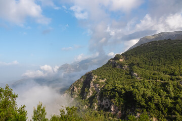 Breathtaking mountain landscape of Ceraunian mountains seen from Pilur in Himare, Albania. Covered in lush green forests, and the sky is clear blue with fluffy white clouds. Mist hangs low in valleys