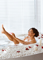 Pretty black young woman shaving her sexy legs while taking bath at home, free space