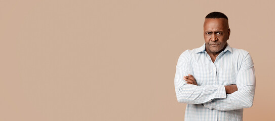 Sulky face. Grumpy mature african american man looking at camera with crossed hands, orange background