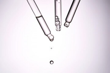 Three pipettes with a cosmetic product. Serum or fluid drips from one of them.