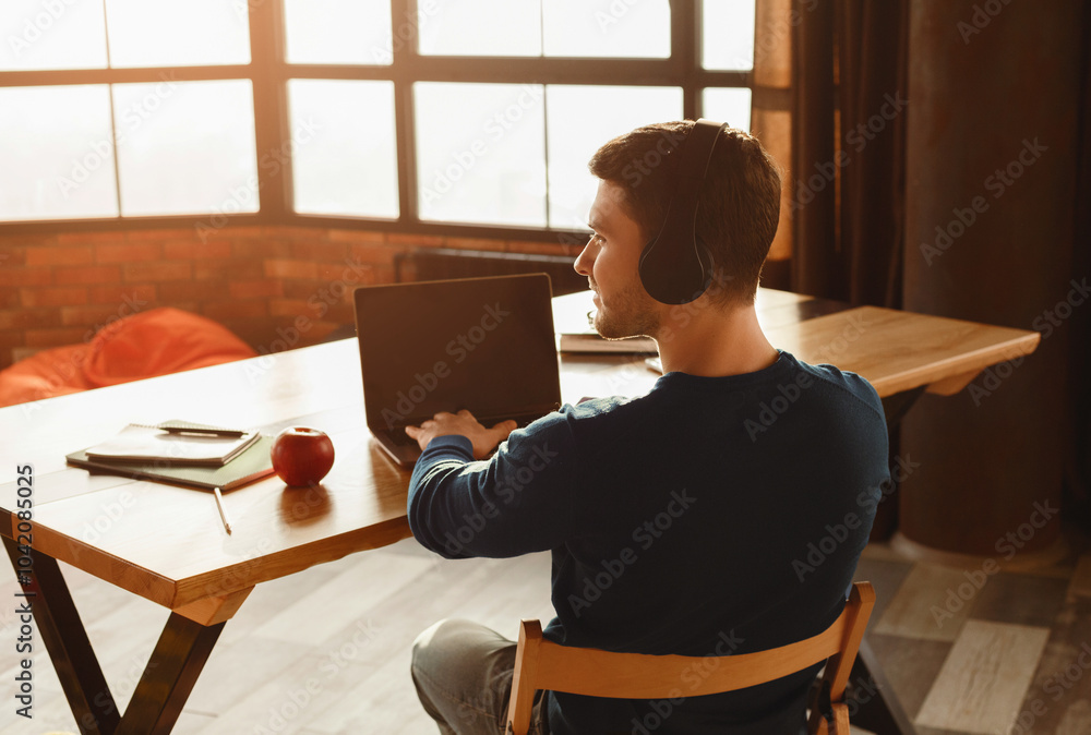 Poster unrecognizable freelancer in headphones working on laptop computer sitting in coworking workspace. b