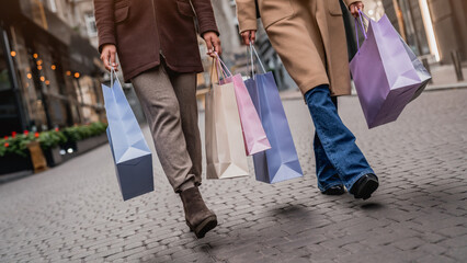 Cropped front view of young women with shopping bags walking along the street. Two girlfriends...