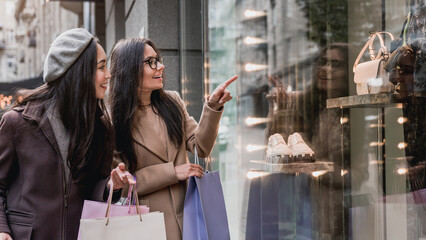 Two young beautiful women females girlfriends enjoy shopping while pointing finger in the shopwindow. Discount and sale, black friday. Shopping for clothes.