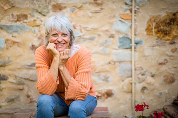 Senior woman smiling and resting her chin on hands while sitting outdoors