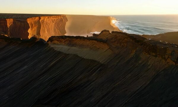 Pan shot with soft, late afternoon light: The camera starts with a close-up of a subduction zone, capturing the interaction between the descending oceanic plate and the continental plate. It then pans