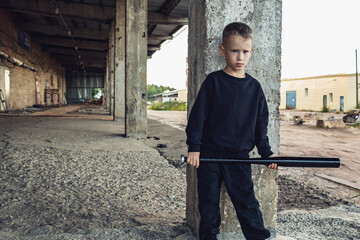 A bLittle boy in black with a baseball bat.oy in black clothes with a baseball bat in his hands.