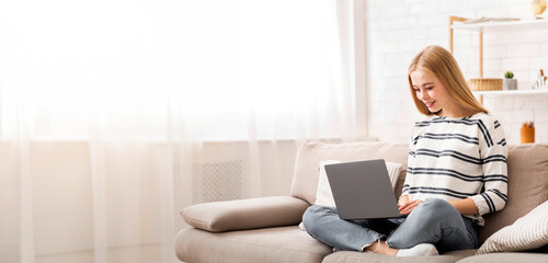 Naklejka premium Looking for job. Student girl using laptop, sitting on couch, home interior, copy space