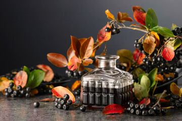 Black chokeberry juice or liquor and fresh berries on a black background.