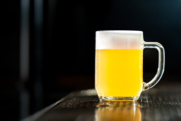 Glass of light beer standing on bar with dark background