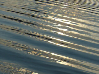 Surface of water and texture of gentle waves and reflections of sunlight during sunset - natural background. Topics: pattern, abstraction, nature, sea water, ocean water, lake water, peace