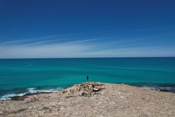 Scenic picture of a man looking at the horizon in front of the ocean. Beautiful viewing spot from the cliffs, endless blue ocean, waves and clear sky. Holidays in south west Australia.