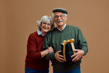 Happy senior couple holding black colored gift boxes with golden ribbon while looking at camera