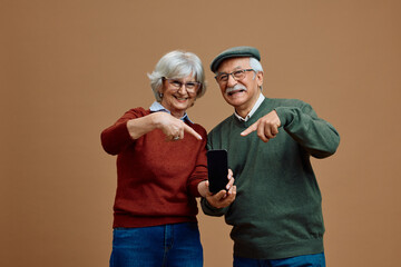 Happy senior couple pointing at  mock-up of a smart phone and looking at camera