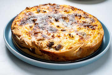 Traditional French pie. Quiche Lauren on a white kitchen table on a blue plate.