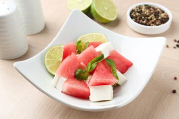 Tasty salad with watermelon, feta cheese, lime and mint on wooden table