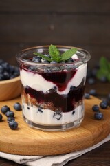 Tasty trifle dessert. Blueberries, sponge cake and whipped cream in glass on wooden table