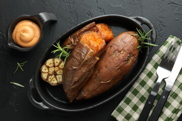 Tasty cooked sweet potatoes served with rosemary and sauce on black table, top view