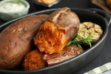 Tasty cooked sweet potatoes, rosemary and garlic on black table, closeup