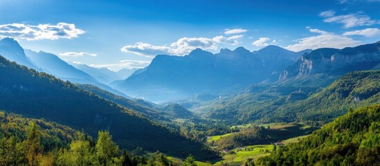 Panoramic view of a mountain valley with lush green forests and blue sky.