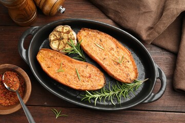 Halves of tasty cooked sweet potato in baking dish served on wooden table, flat lay