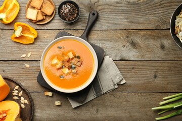 Delicious pumpkin soup in bowl and ingredients on wooden table, flat lay