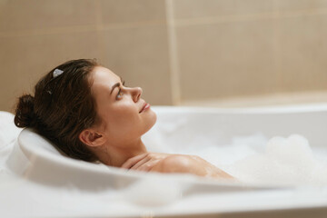 Relaxed woman enjoying a bubble bath in a cozy bathroom, with soft lighting creating a calming atmosphere. Self-care and wellness concept.