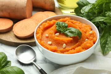 Tasty mashed sweet potato with basil, seeds in bowl and ingredients on table, closeup