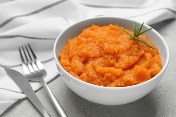 Tasty mashed sweet potato with rosemary in bowl served on grey textured table, closeup