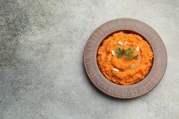 Tasty mashed sweet potato with pumpkin seeds and parsley in bowl on gray textured table, top view. Space for text