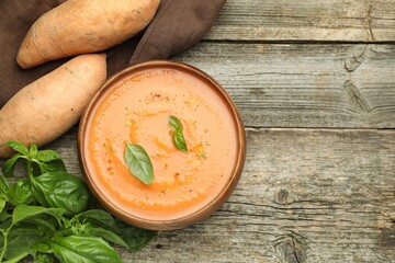 Delicious sweet potato soup with spices in bowl, fresh vegetables and basil on wooden table, flat lay. Space for text