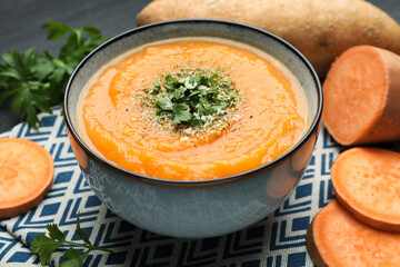 Delicious sweet potato soup with parmesan cheese in bowl and fresh ingredients on table, closeup