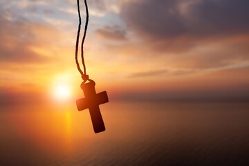 Person pray with bead rosary with cross at sunset.