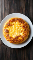 Appetizing omelette on a white plate against a wooden surface, top-down view. Vibrant yellow hues pop against rustic backdrop, promising a delicious meal