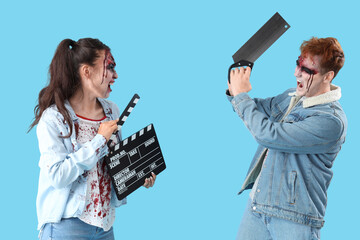 Young couple dressed for Halloween as zombies with movie clapper on blue background