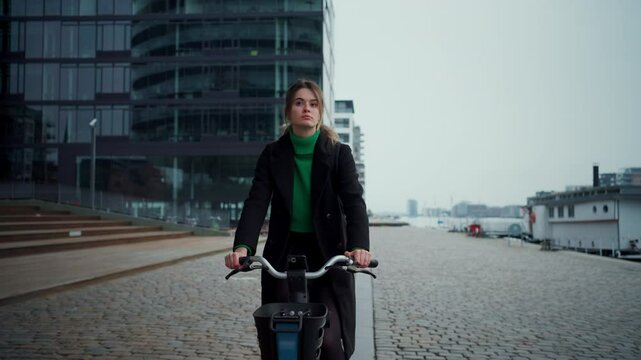 Focused woman riding bicycle at empty walkway along river and using navigator at autumn day