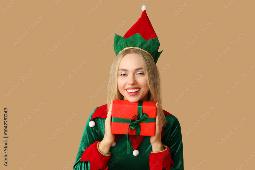 Wall mural beautiful young woman in elf costume with christmas gift box on brown background