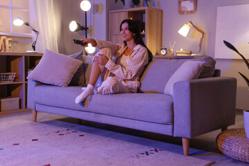 Beautiful young woman watching TV at home in evening
