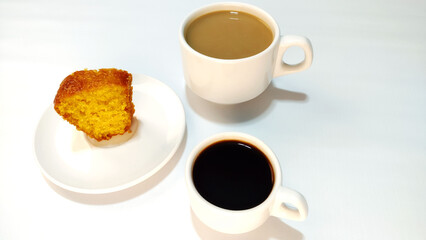 Piece of cornmeal cake, cup of coffee, cup of coffe with milk also known as latte.
