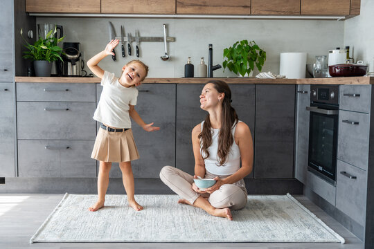 Mother and daughter sitting on kitchen floor, eating or having a breakfast and playing. Family bonding