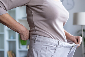 Woman demonstrates significant weight loss success holding waistband of loose pants. Celebratory...