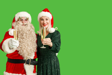 Santa Claus and beautiful mature woman in Christmas hats with glasses of champagne on green background