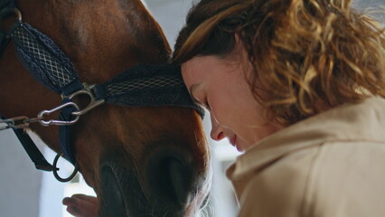 Woman stallion love moment at barn closeup. Happy equestrienne bonding to horse