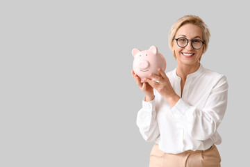 Happy mature woman with pink piggy bank on grey background