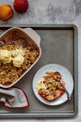 Crumble, Crisp or Cobbler with nectarines, peaches, rolled oats and scoop of ice cream in casserole dish on a metal tray. American cuisine. Easy dessert.